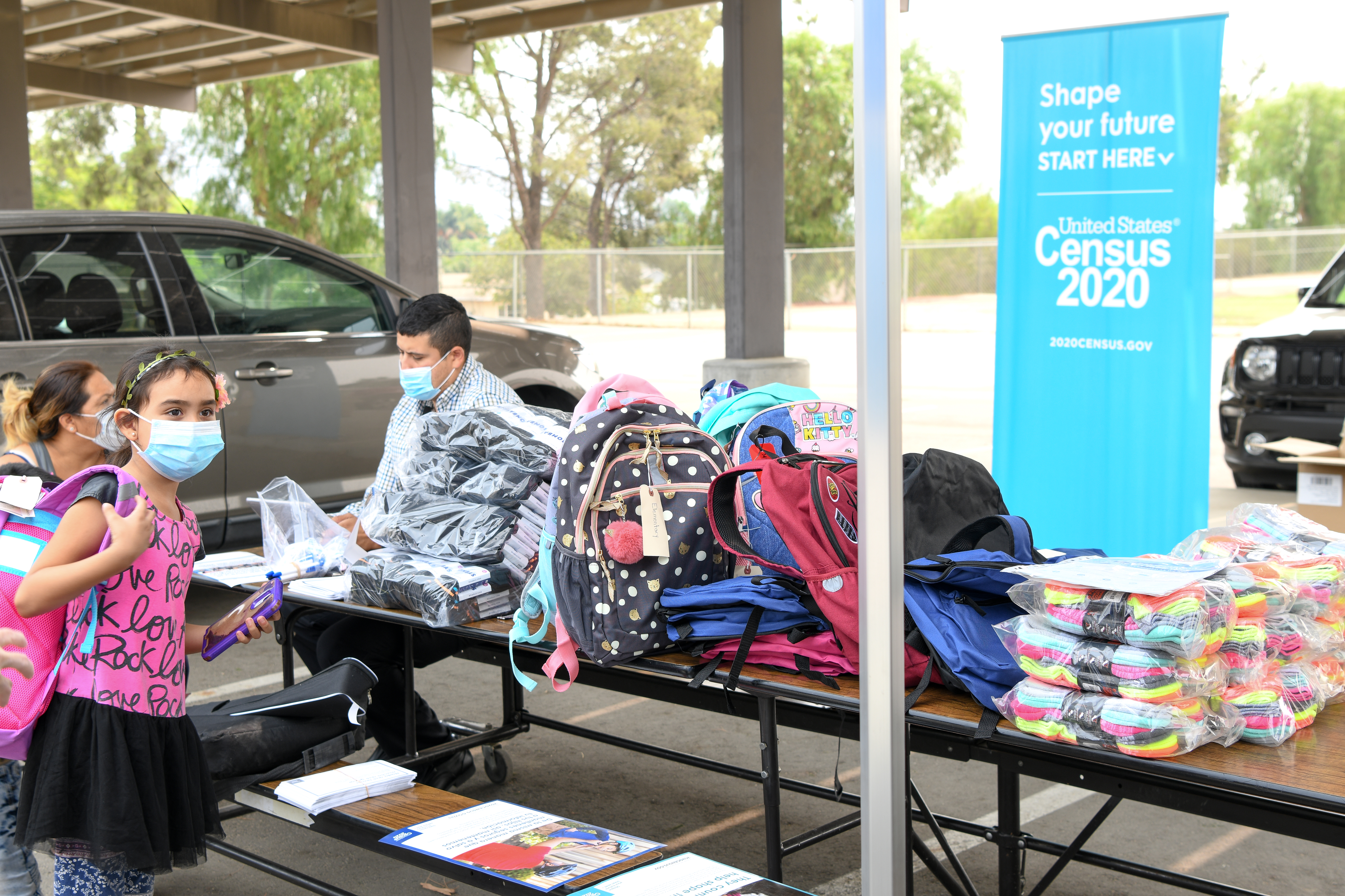 A man sits behind a table with backpacks to hand out to families completing the 2020 Census.