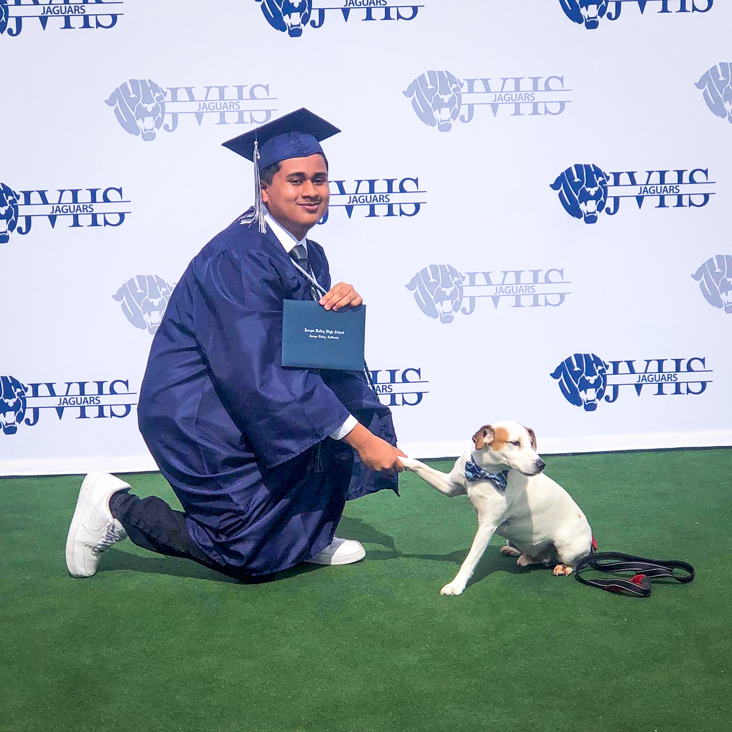 JVHS graduate shakes paw of dog while holding diploma