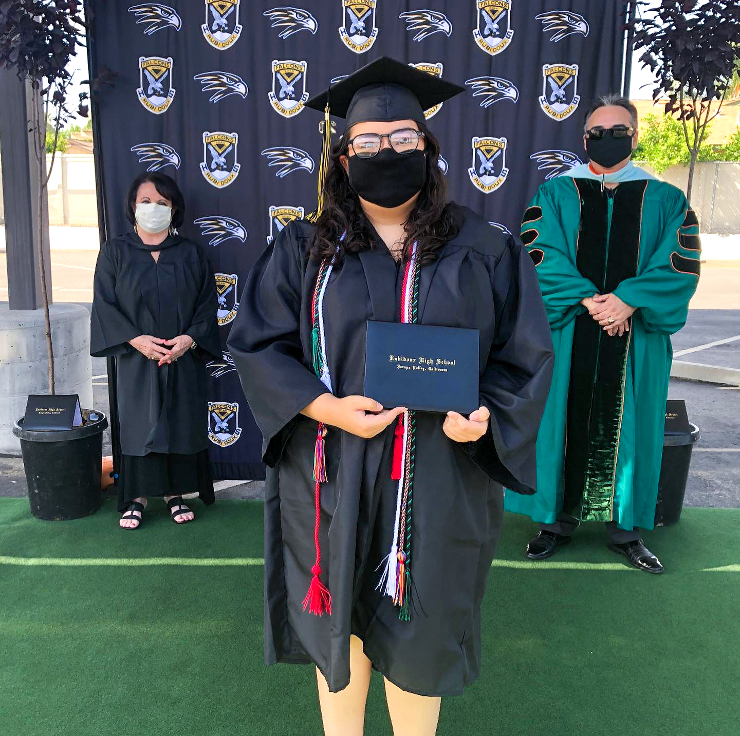 RHS graduate wearing a mask holds diploma; two others in masks stand behind her