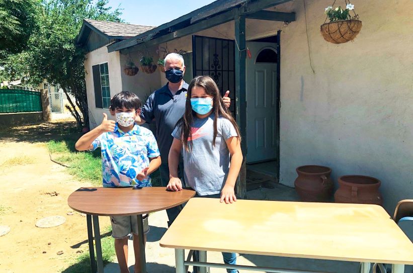 A man and two kid wearing masks stand behind donated desks