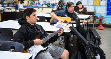 three students in a row playing guitar